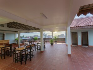 A spacious patio area with tiled flooring, wooden tables and chairs, potted plants, and a view of the cityscape.