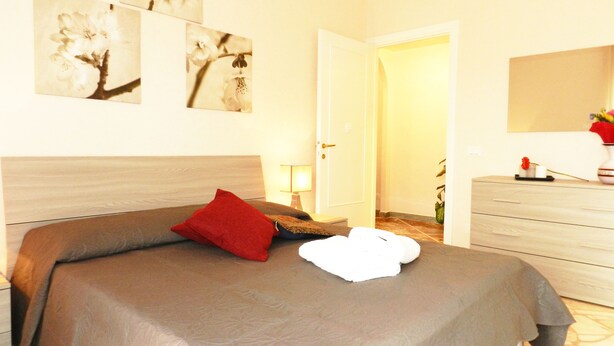 Un dormitorio con cama, mesita de noche, lámpara, cómoda y cuadros en la pared.