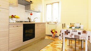 Una cocina compacta con estufa, horno y pileta, una mesa de comedor con sillas, y un ventanal con cortinas.