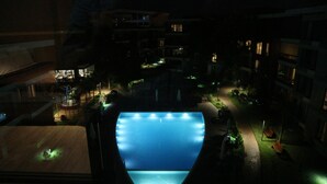 Vista noturna de um pátio de hotel com piscina, iluminado por luzes artificiais.