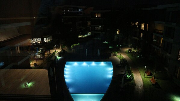 A nighttime view of a hotel courtyard with a pool, illuminated by artificial lighting.