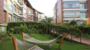 Pátio com rede, vegetação exuberante e edifícios de apartamentos modernos.