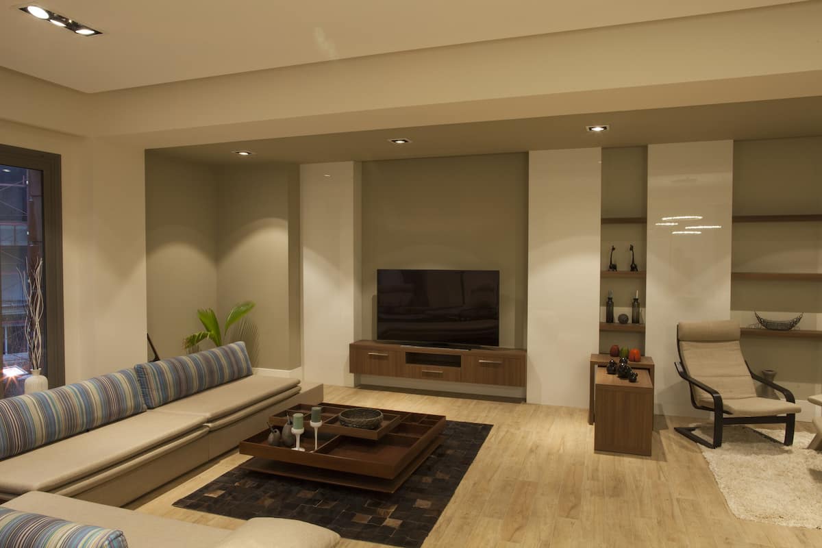 Een moderne woonkamer met een grote flatscreen televisie, een bank met gestreepte kussens, een salontafel en een fauteuil.