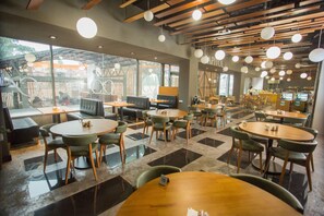 A modern cafe with round tables and green chairs, large windows, and a wooden ceiling.