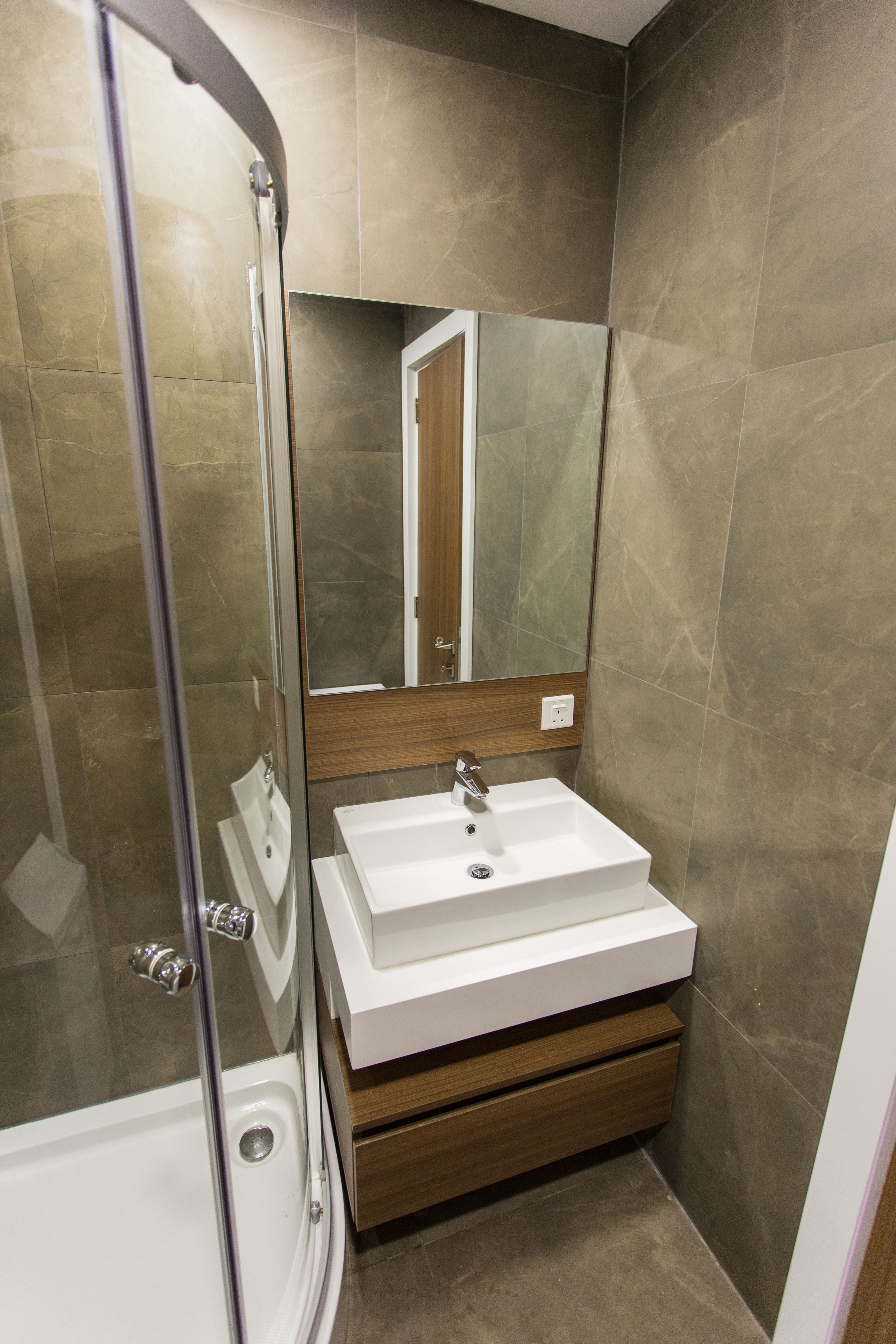 A modern bathroom with a glass shower enclosure, a white sink, and a wooden vanity.