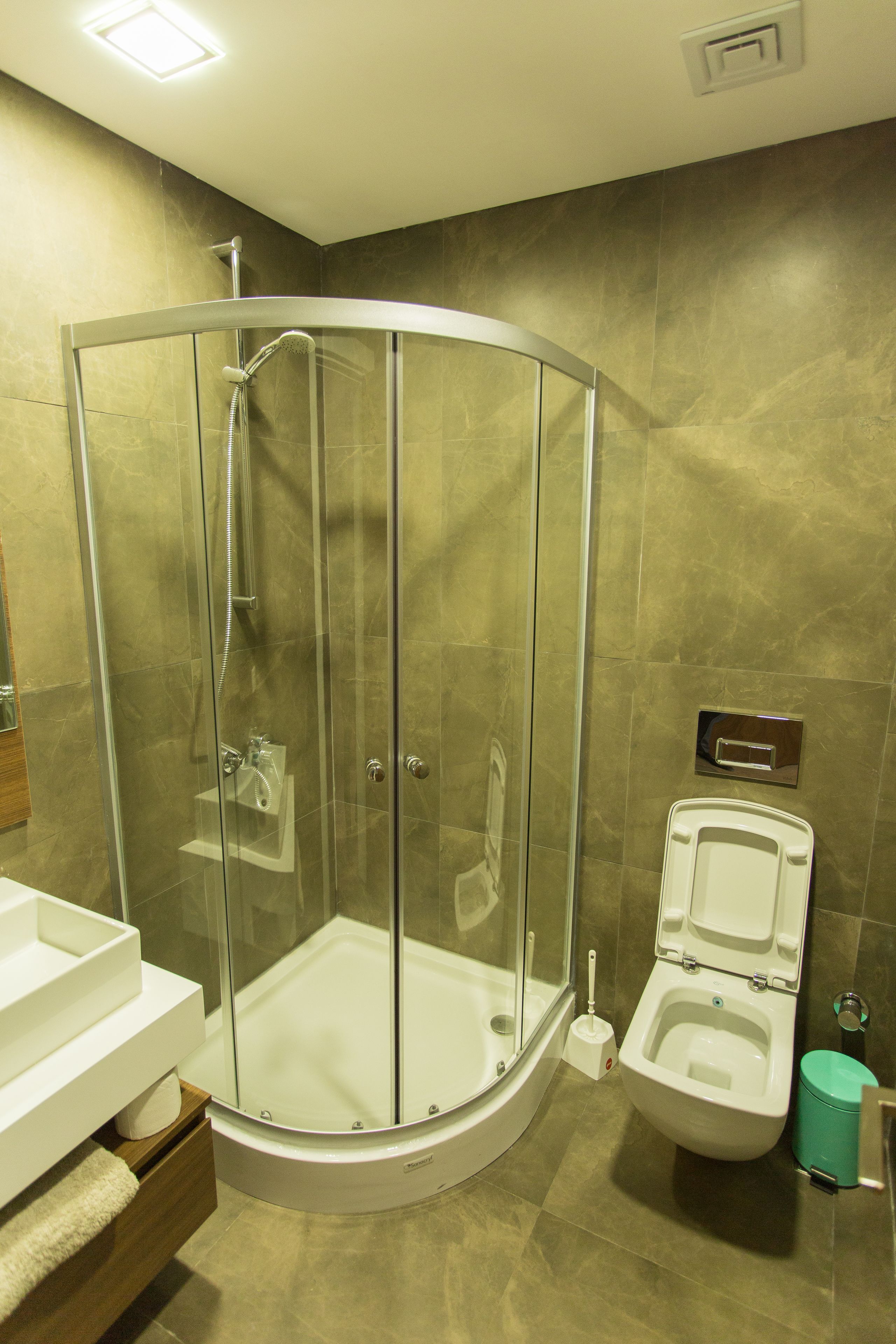 Een moderne badkamer met een douchecabine van glas, een wit toilet en een wastafel met een houten meubel.