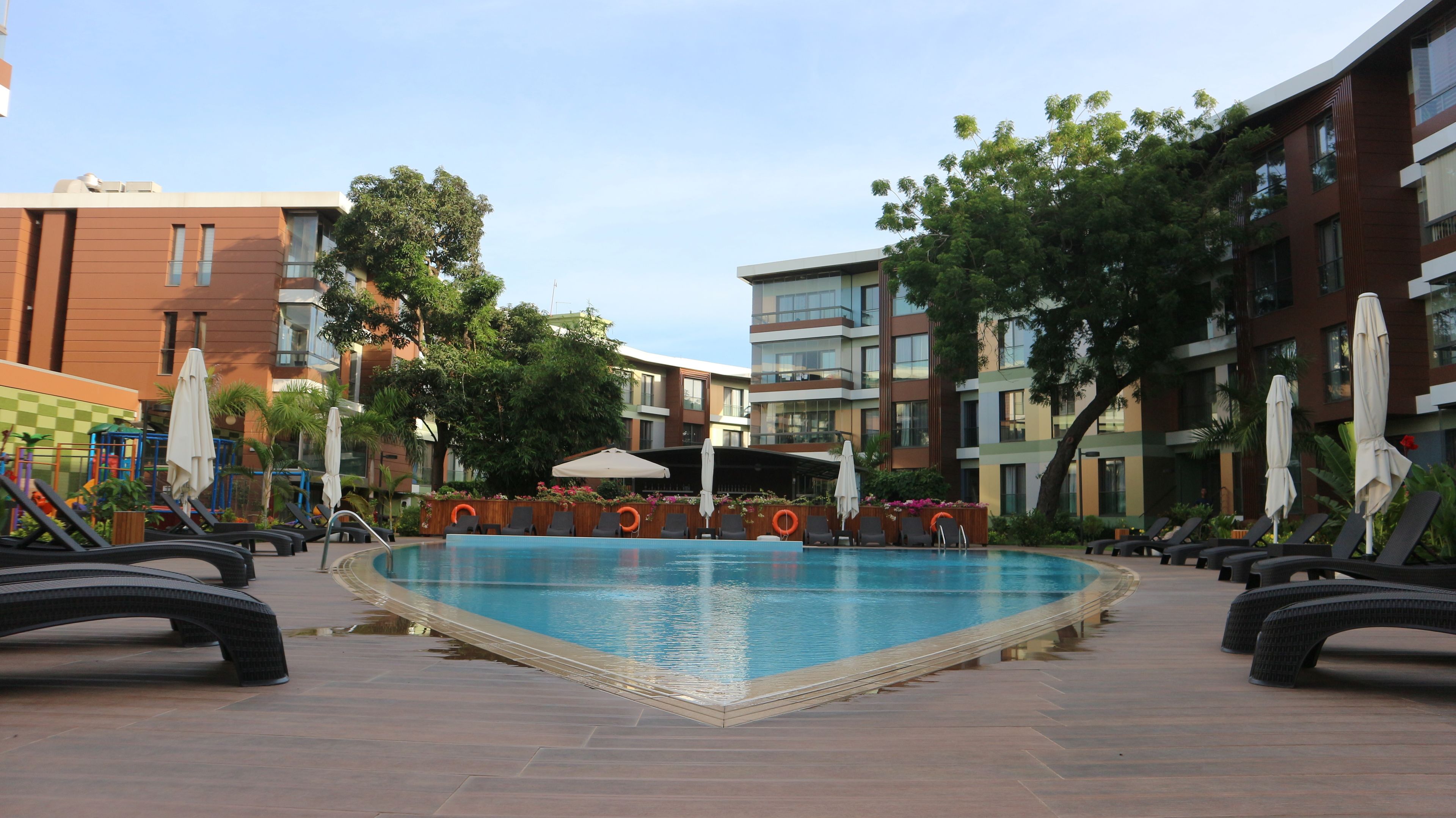 A swimming pool with lounge chairs and umbrellas, surrounded by multi-story buildings with balconies.