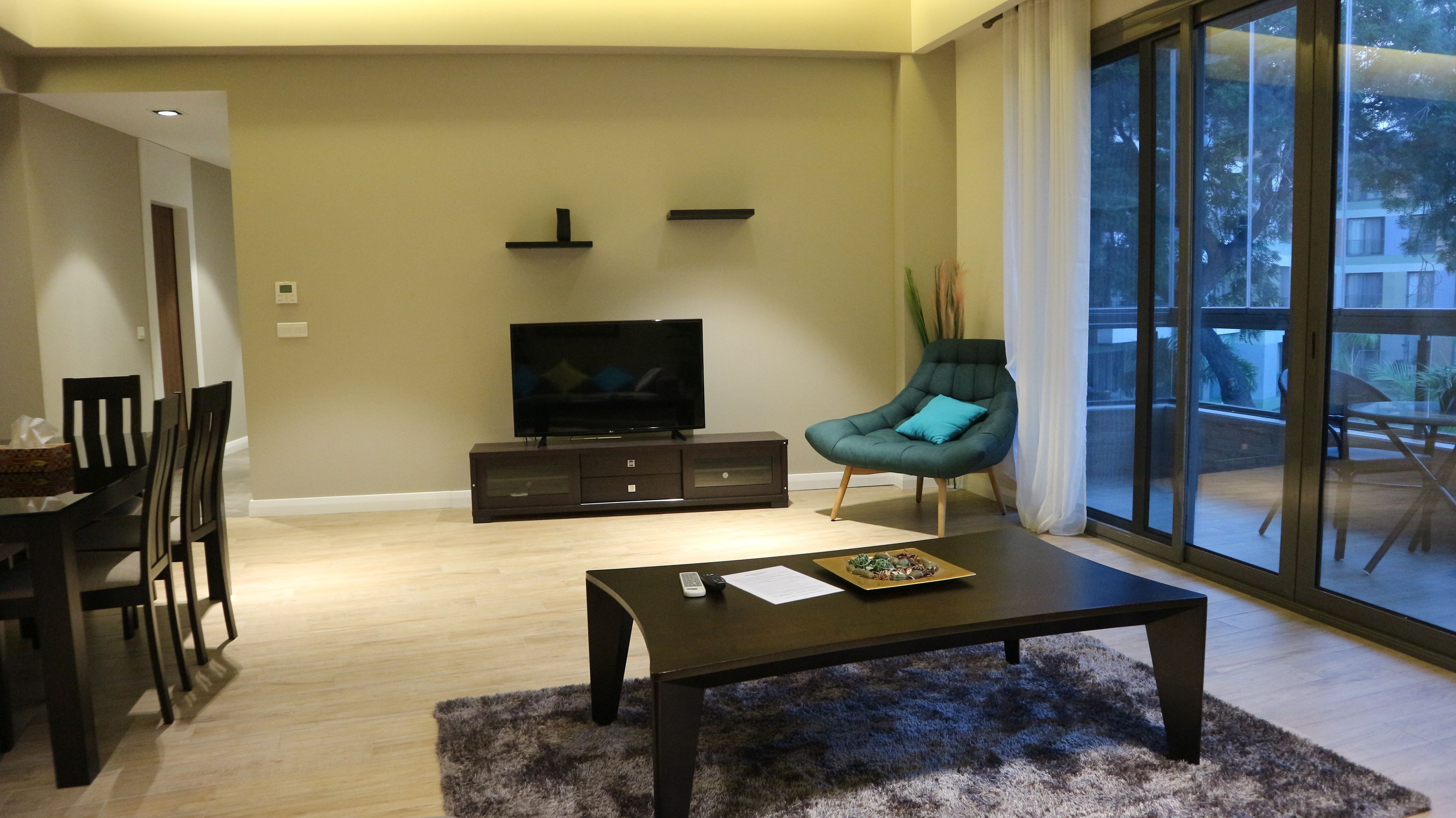 A modern living room with a flat-screen TV, a dark wooden coffee table, and a teal armchair.
