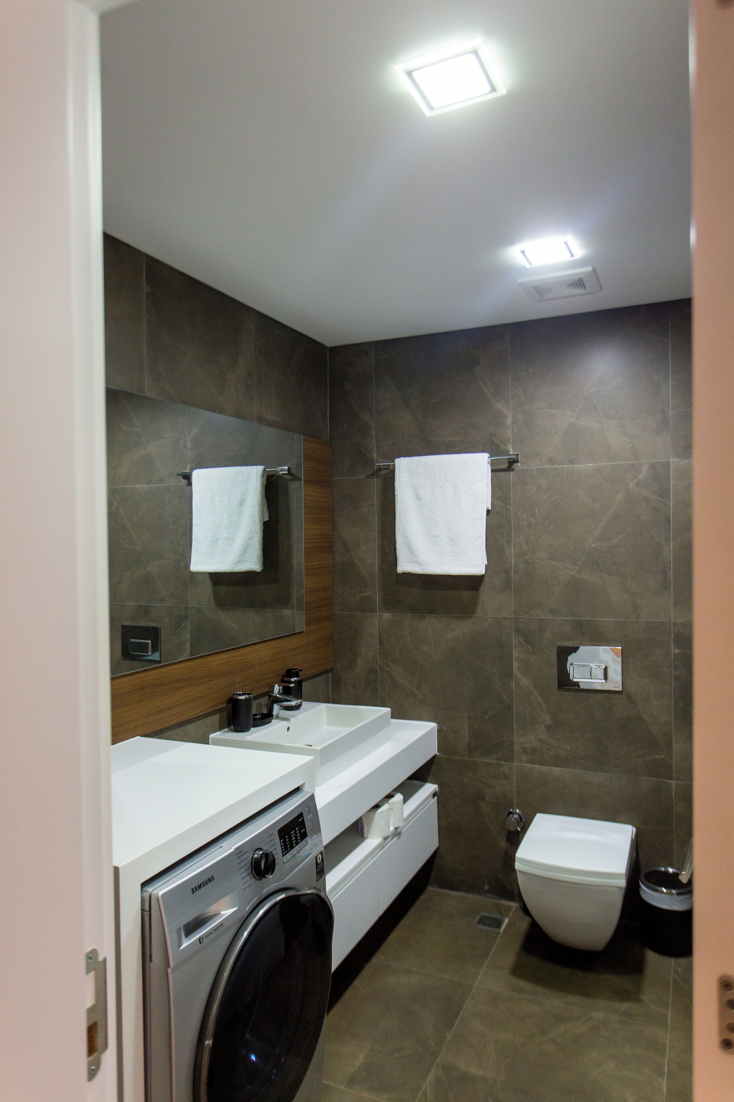 Een moderne badkamer met een wasmachine, een wastafel, een spiegel en een toilet.
