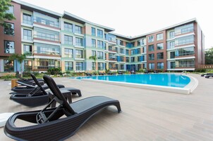 A modern hotel with a swimming pool, lounge chairs, and a multi-story building with balconies.