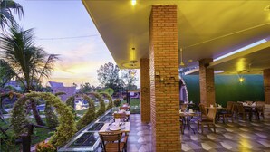 An outdoor dining area with brick pillars, geometric patterned flooring, and a view of the cityscape at sunset. - Garden Flower Resort (Siem Reap)