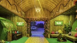 A room with a green carpet, wooden walls, and a wooden ceiling. There is a sofa, a coffee table, and a plant. - Garden Flower Resort (Siem Reap)