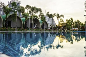 A swimming pool with a clear reflection of palm trees and a building with curved green roofs. - Garden Flower Resort (Siem Reap)