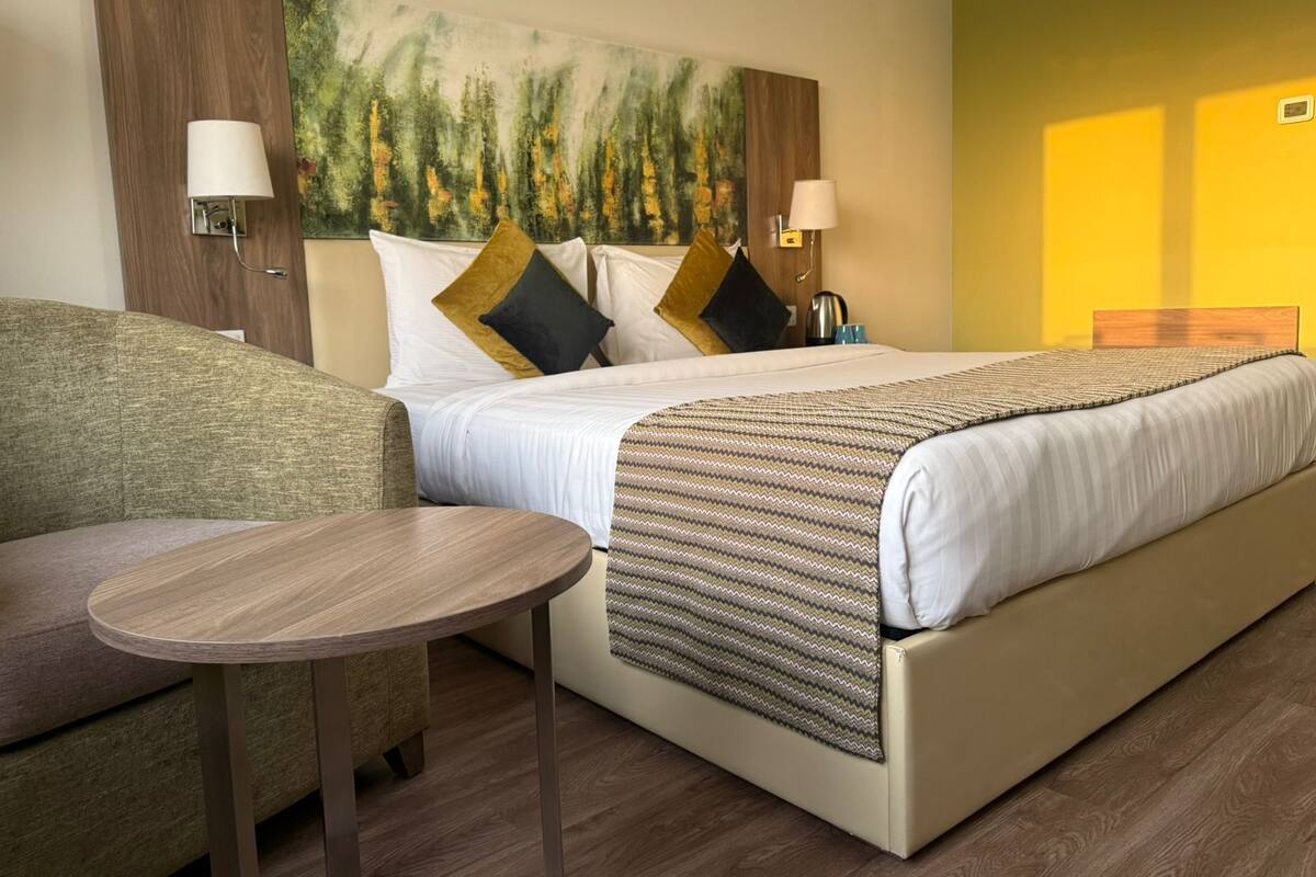 Hotellihuone, jossa on sänky, sohva, pieni pöytä ja taulu seinällä.