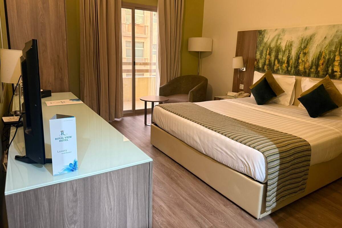 Hotellihuone, jossa on suuri sänky, työpöytä tietokoneella, tuoli, pieni pöytä ja taulu seinällä.