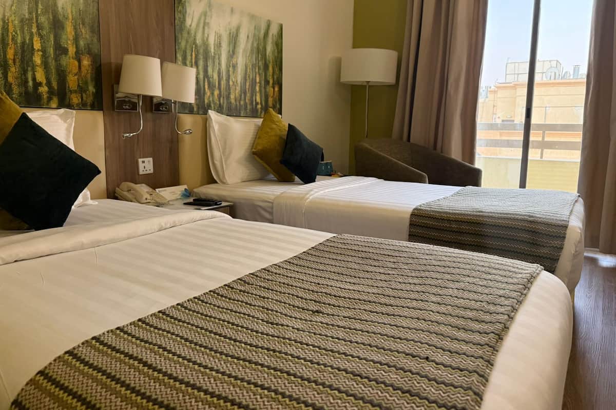 Hotellihuone, jossa on kaksi sänkyä, suuri ikkuna ja taulu seinällä.