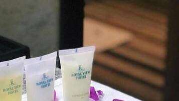 Three Royal View Hotel bath products on a table with a towel and pink flower petals.