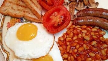 A breakfast plate with eggs, toast, tomatoes, mushrooms, sausages, and beans.