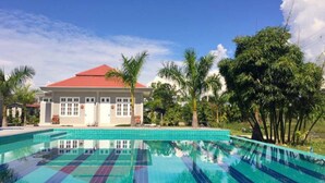 A swimming pool with a tiled pattern, surrounded by palm trees and a building with a red roof. - Ativara Hotels And Resorts (Nyaungshwe)