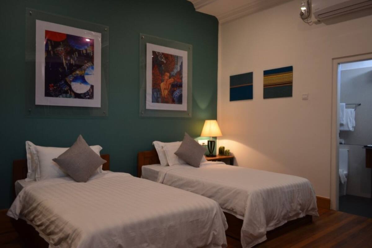 A hotel room with two beds, a nightstand with a lamp, and artwork on the walls.