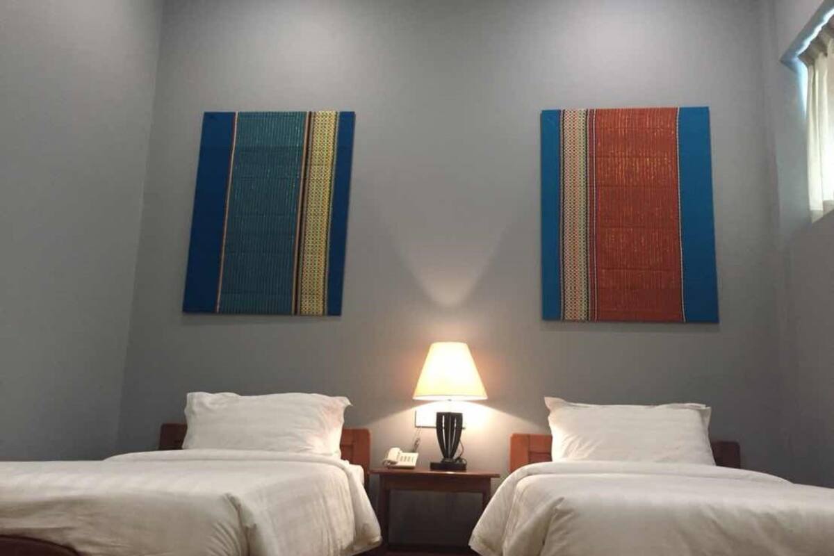 A hotel room with two beds, a nightstand with a lamp, and two abstract paintings on the wall.