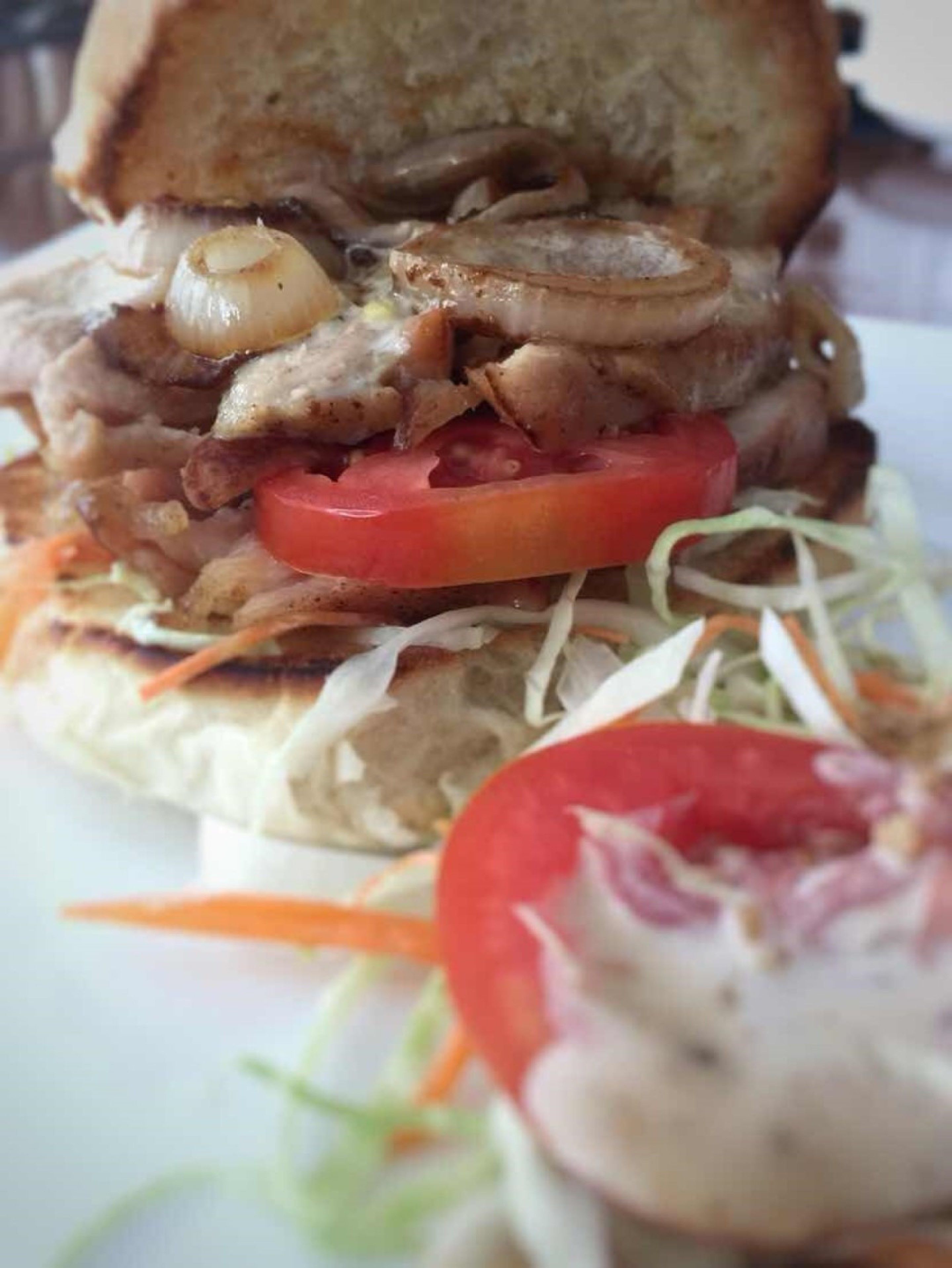 A sandwich with visible layers of meat, tomato, and onions on a bun, accompanied by a side salad.