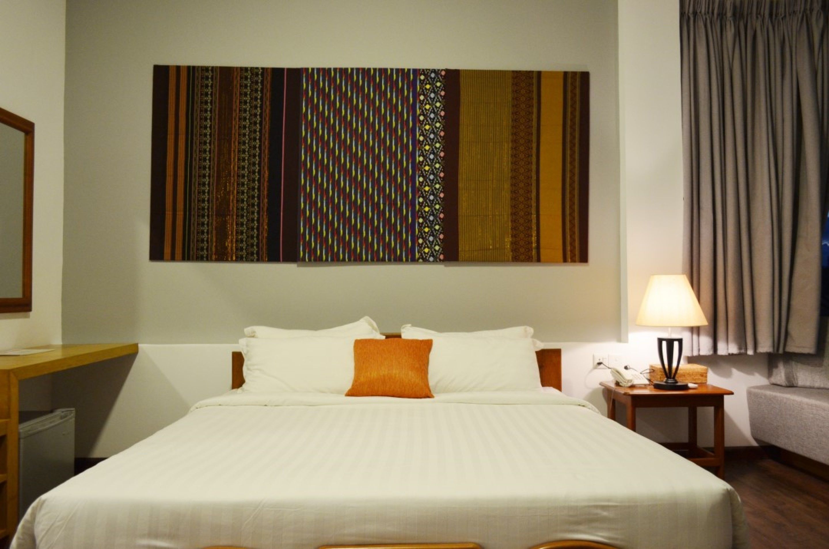 Una habitació d'hotel amb un llit gran, una taula de nit amb una làmpada, una taula petita amb un telèfon i un quadre abstracte gran a la paret.
