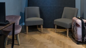 A room with a blue wall, a large black headboard, two patterned chairs, a small pink chair, a wooden desk with a computer, and a suitcase. - Maison Brunetti (Rome)
