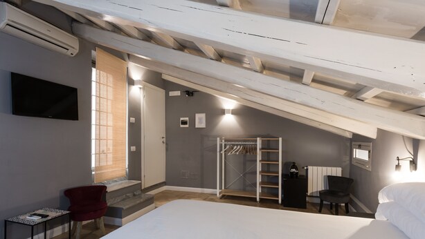 A bedroom with a large bed, a red chair, a TV, a wardrobe, and a window with blinds. - Maison Brunetti (Rome)