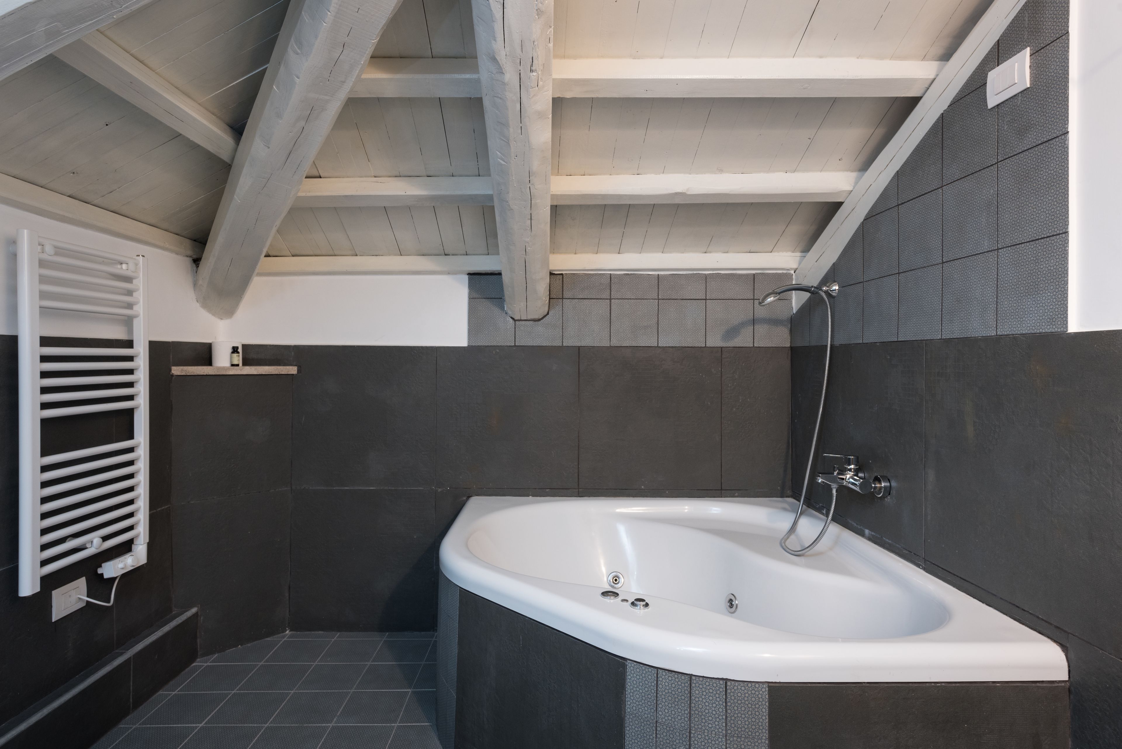 A modern bathroom with a freestanding bathtub, dark tiled walls, and a wooden ceiling.