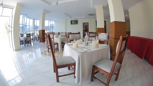 Zona pranzo con tavoli rotondi, sedie di legno e tovaglia rossa.