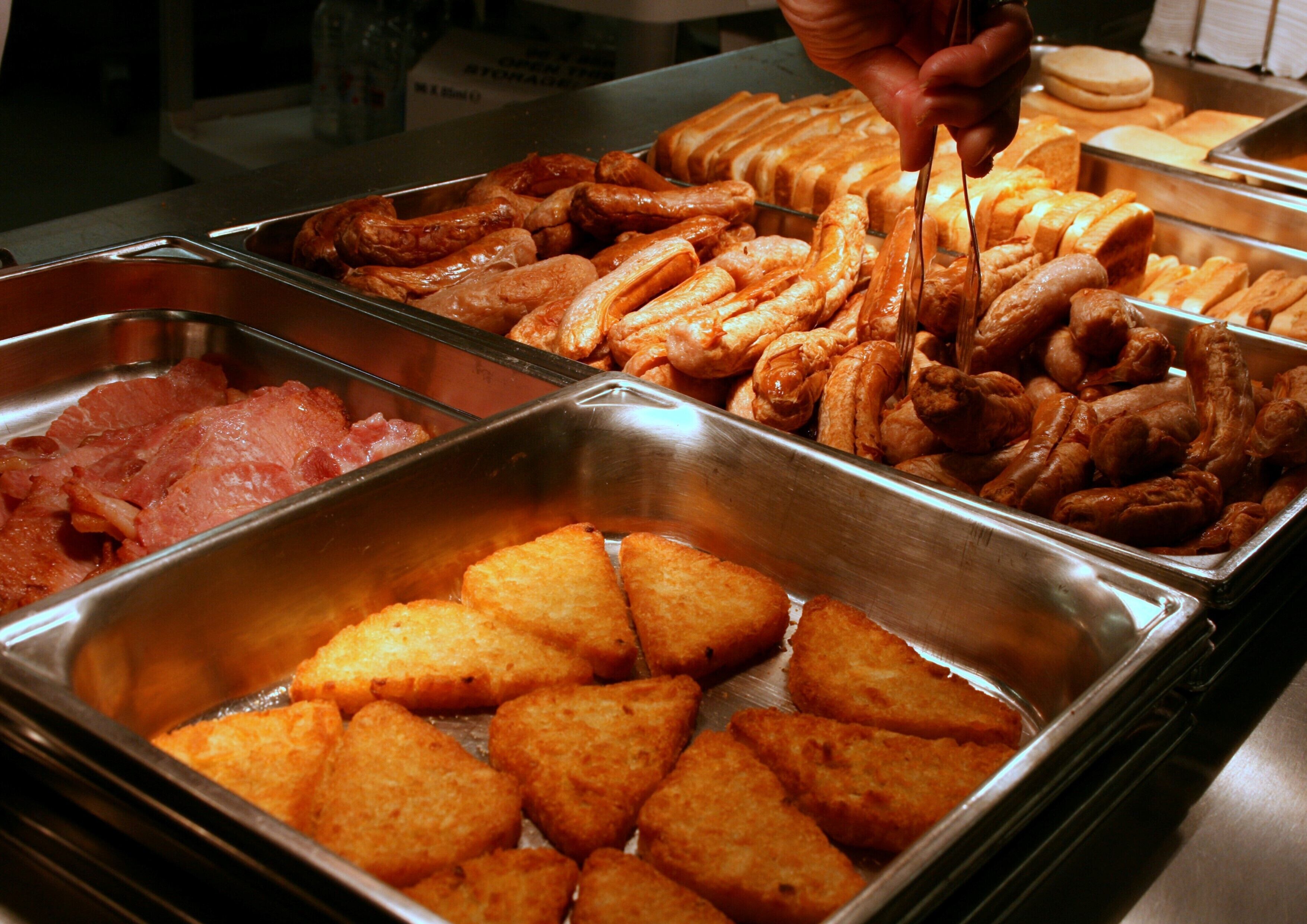 Un bufé con diferentes opciones de comida, incluyendo salchichas, pasteles y alimentos fritos.
