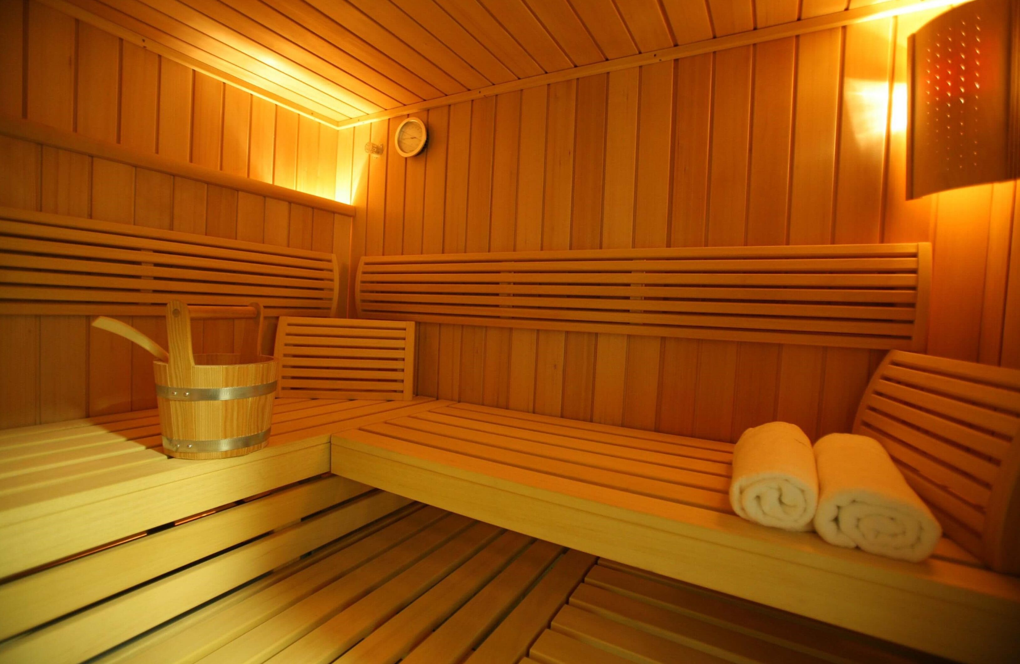 A sauna with wooden benches, a wooden bucket, and towels.