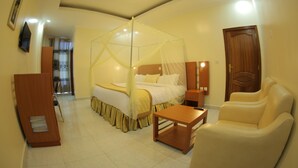 Camera d'albergo con un letto a baldacchino, un angolo salotto con una poltrona, un comodino e una porta in legno.