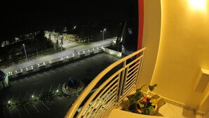 Vista notturna da un balcone su un parcheggio e una strada illuminata da lampioni.
