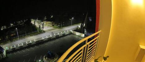 Vista nocturna desde un balcón con vista a un estacionamiento y una calle iluminada.