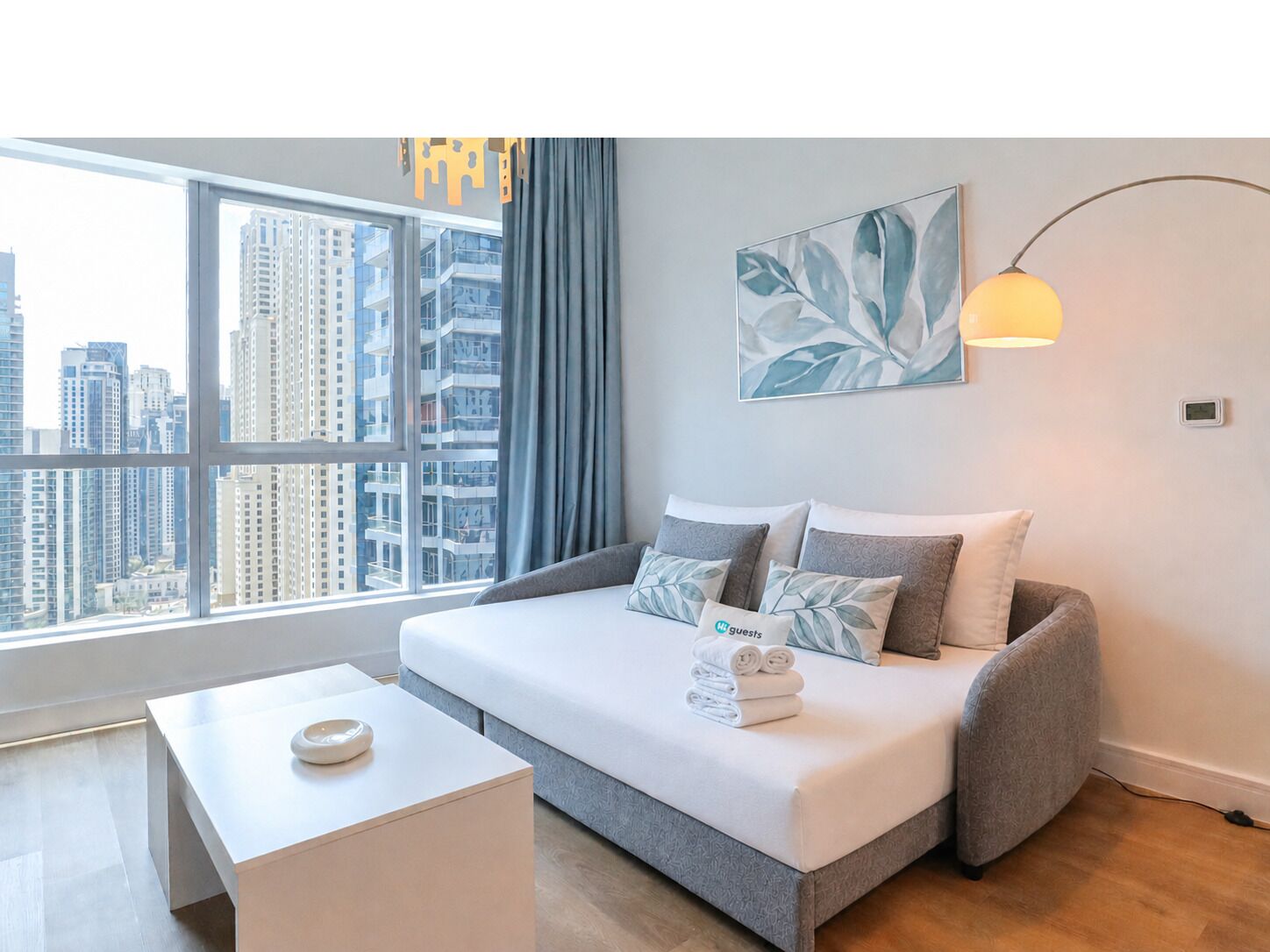Una habitación de hotel moderna con un ventanal grande, un sofá cama, una mesita de noche y una lámpara de pared.