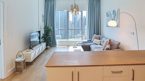 Un salon moderne avec un canapé, un téléviseur, une table en bois et une vue sur de grands immeubles à travers de larges fenêtres.