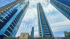Trois immeubles de grande hauteur aux façades en verre réfléchissant, un bâtiment central à l’architecture verticale et un plus petit bâtiment orné d’un logo.