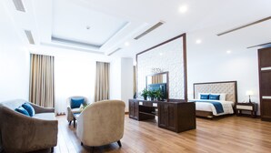 A hotel room with a wooden floor, a sofa, a chair, a bed, a TV, and a desk. - Song Loc Luxury (Bai Chay)