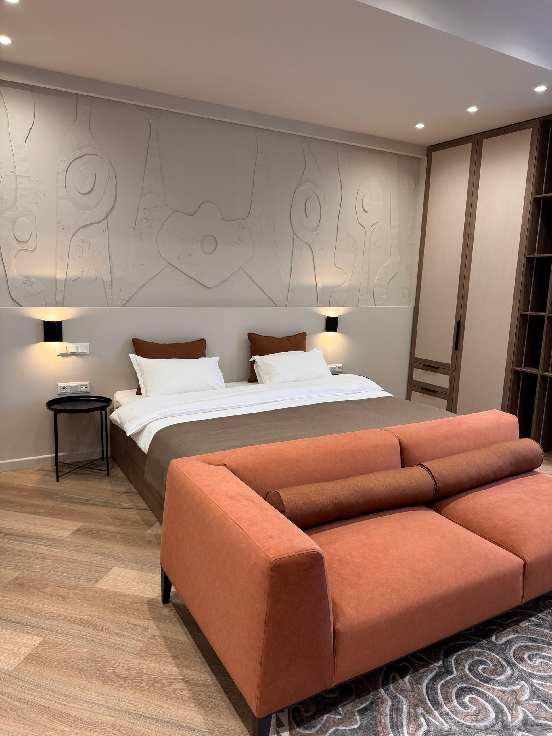 A modern bedroom with a bed, two bedside tables, a sofa, and a patterned rug.