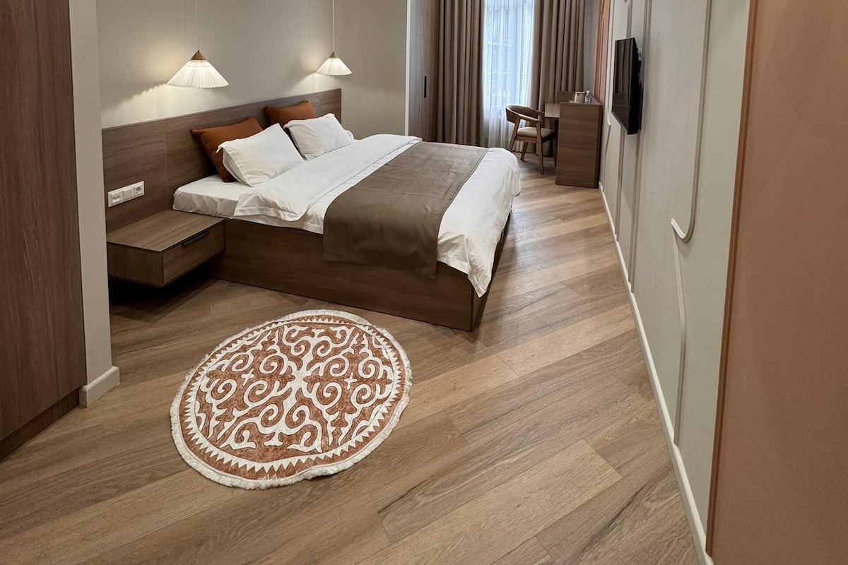 Una habitación de hotel moderna con una cama grande, mesitas de noche, un tapete redondo y una lámpara de techo.
