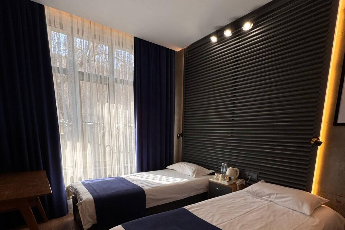 Habitación de hotel con dos camas, suelo de madera, escritorio y ventana con cortinas.