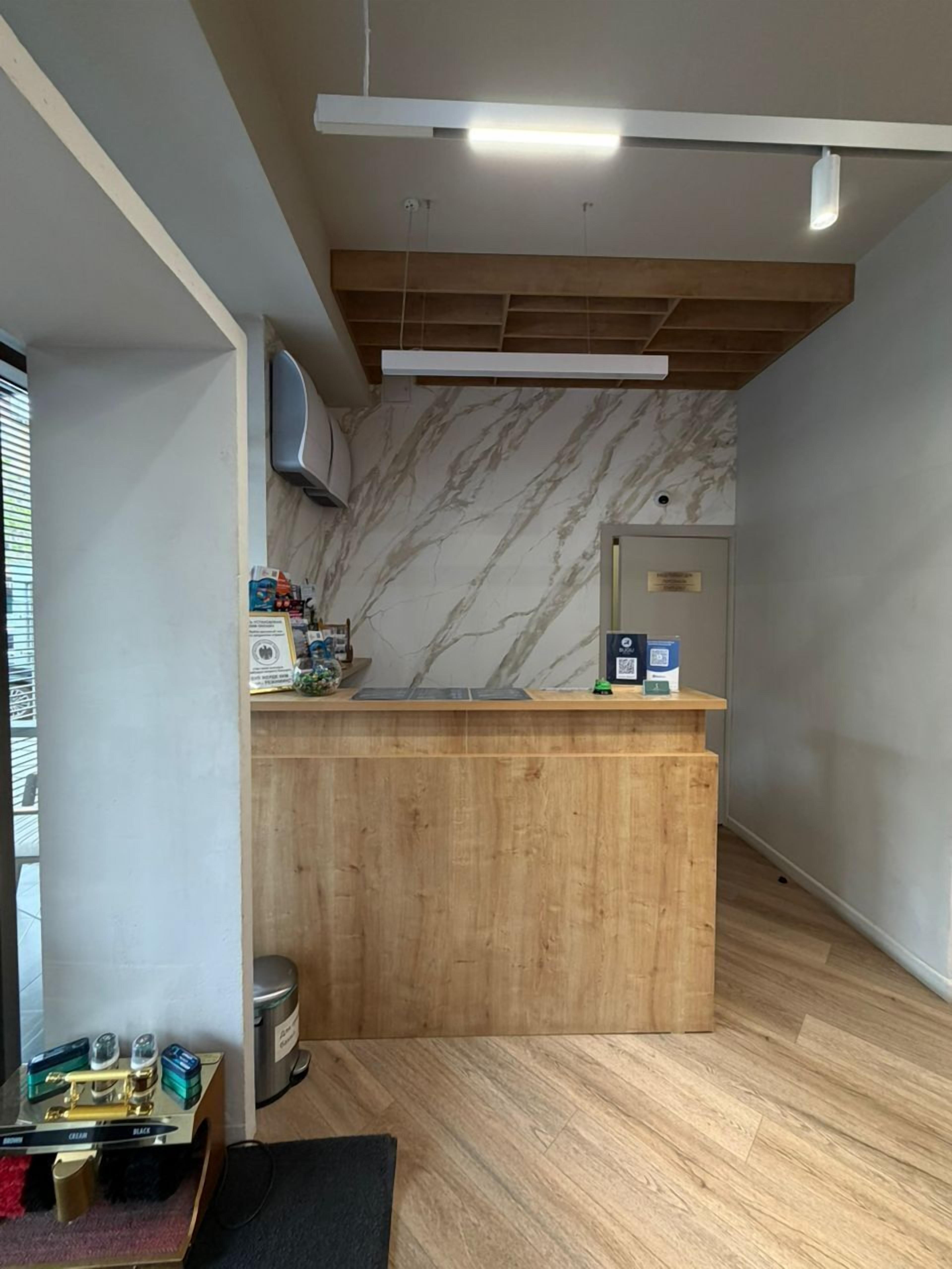 A reception desk with a marble wall, wooden panel ceiling, and a trash bin.
