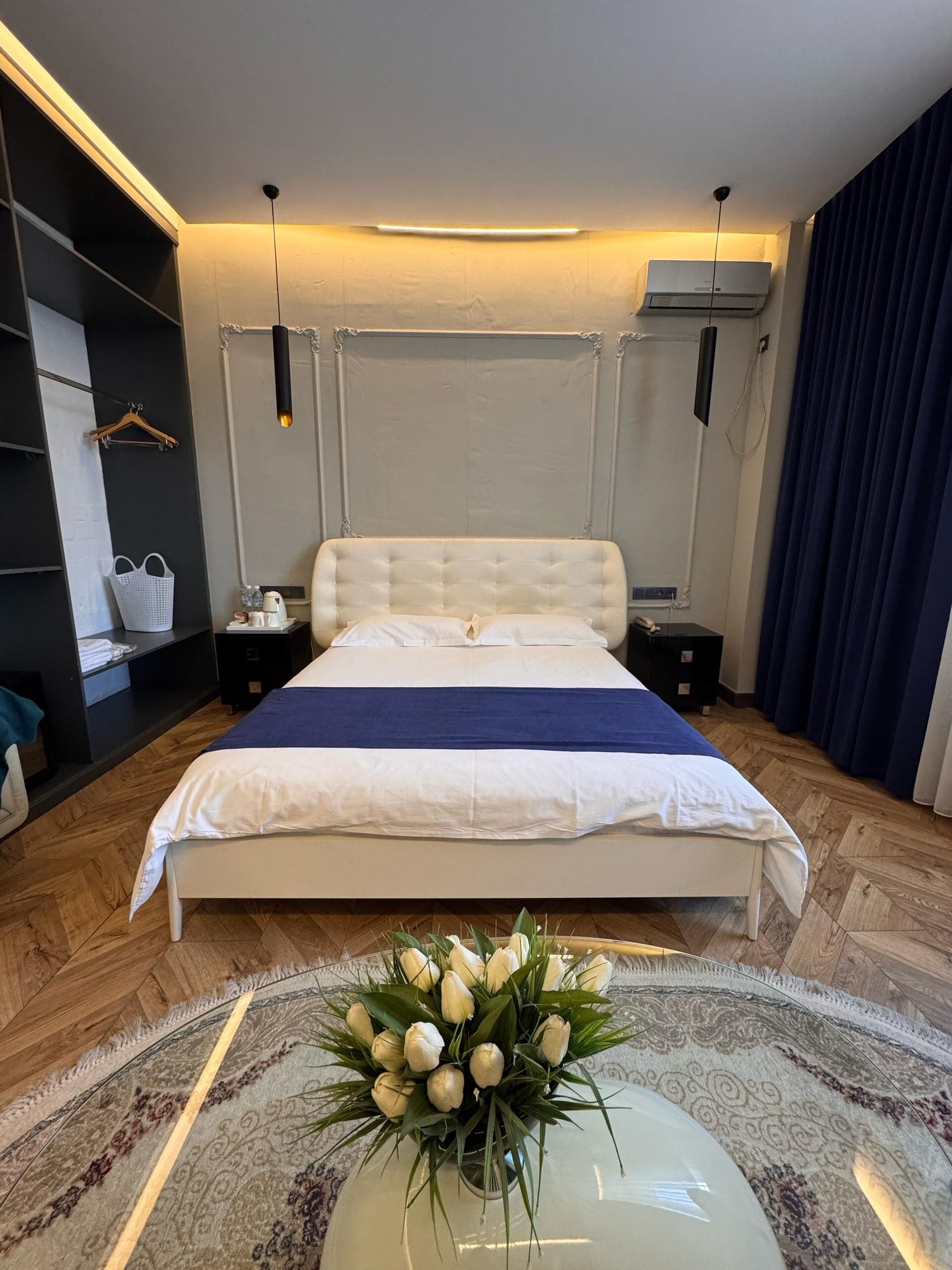 Ett modernt sovrum med en stor säng, sängbord, en garderob och en dekorativ vas med blommor.