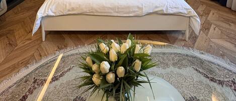 Ett modernt sovrum med en stor säng, sängbord, en garderob och en dekorativ vas med blommor.