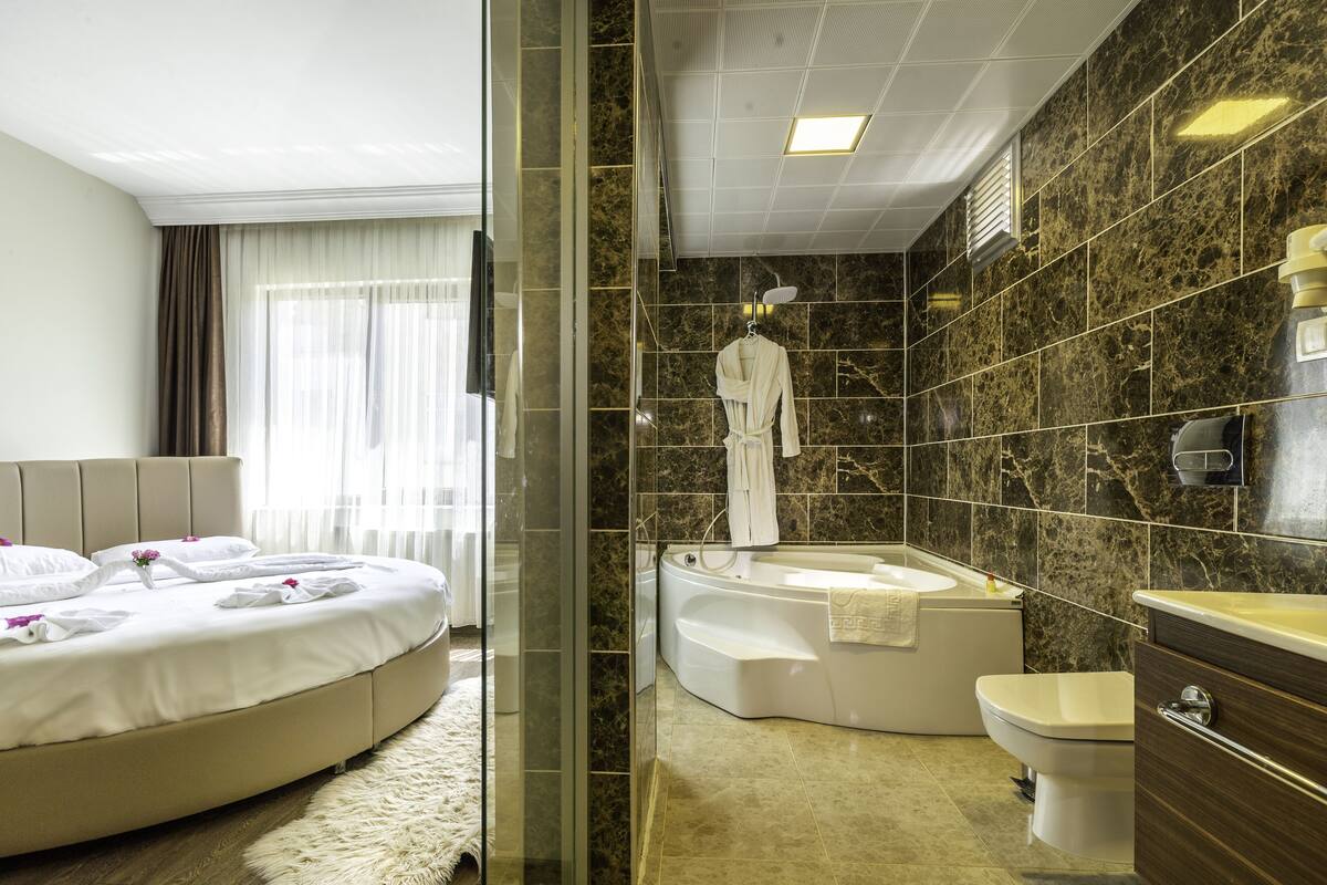 A modern hotel room with a curved bed, a separate bathroom featuring a freestanding bathtub, and a marble-tiled shower area.