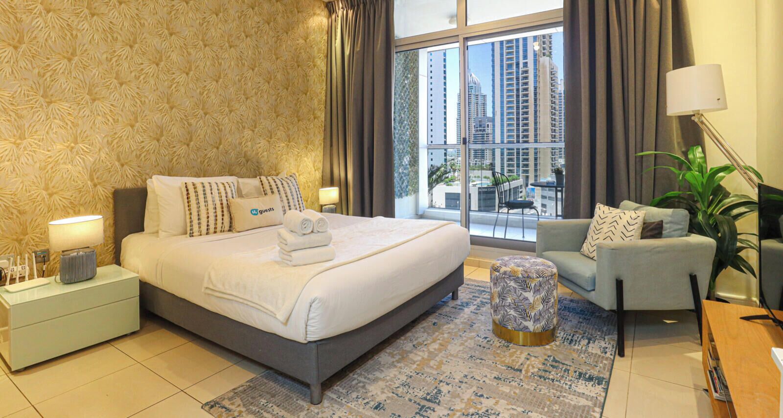 Habitación de hotel con una cama grande, una zona de estar con una silla, una mesa redonda pequeña y vistas de la ciudad a través de la ventana.