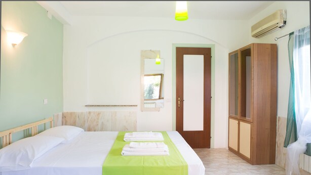 Ein Hotelzimmer mit zwei Betten, einer grünen Bettdecke, einem Holzschrank, einer Tür und einer Klimaanlage.
