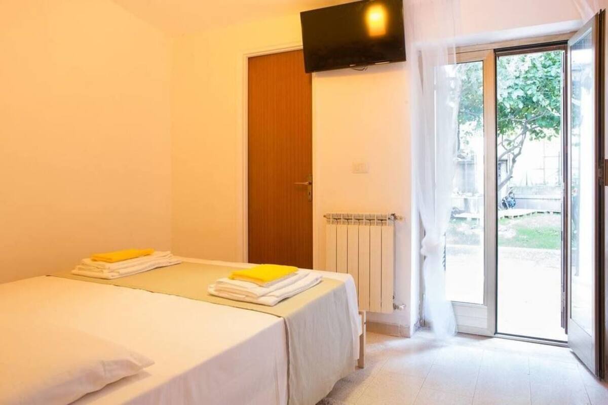 A hotel room with a bed, a TV mounted on the wall, and a sliding glass door leading to an outdoor area.